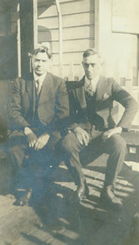 Item #63-2756 Black and white photograph of two men in suits seated in front of a house. 20th Century American Photographer.
